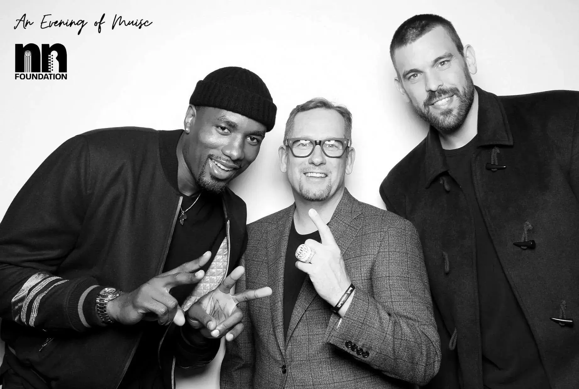 Three men pose before a white backdrop with An Evening of Music and nn Foundation logos; two make peace signs, center wears glasses.